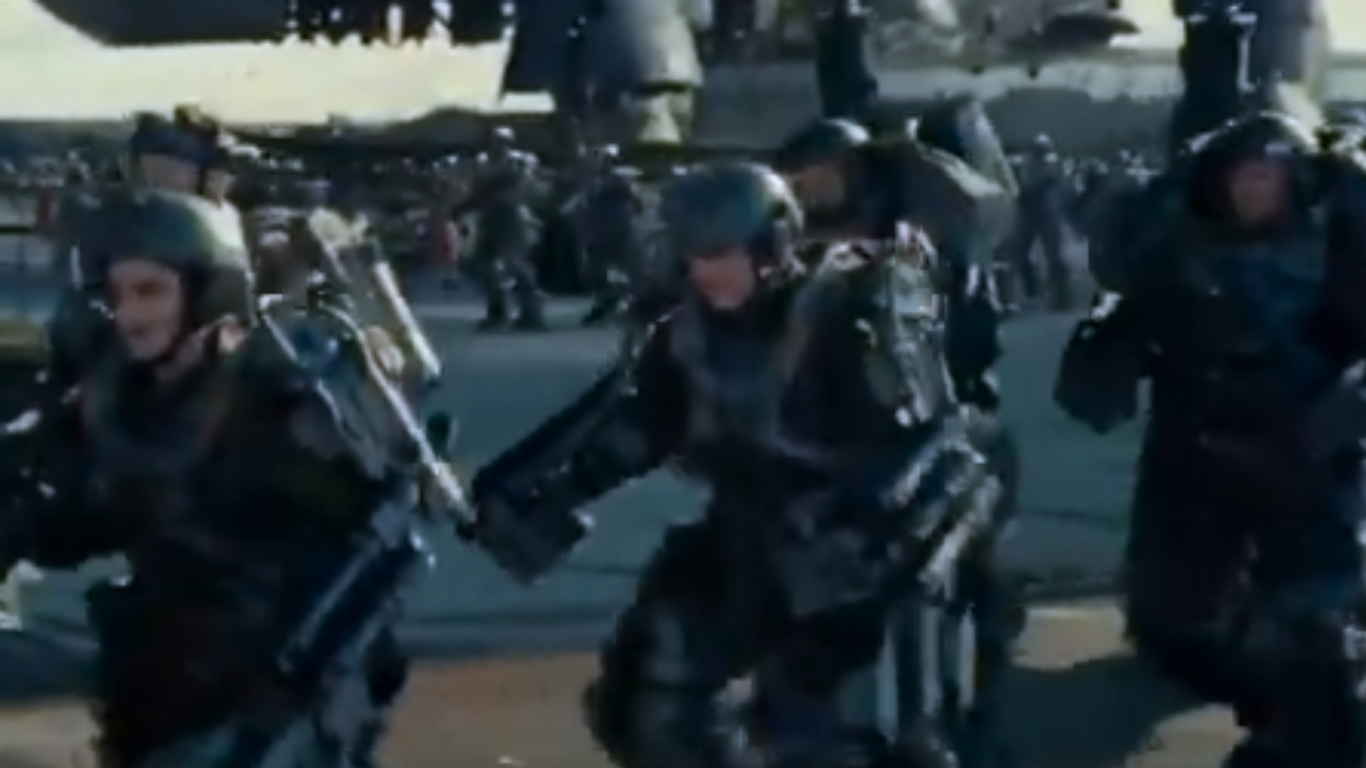 Soldiers wearing advanced powered exoskeleton suits running with heavy equipment near a military aircraft.