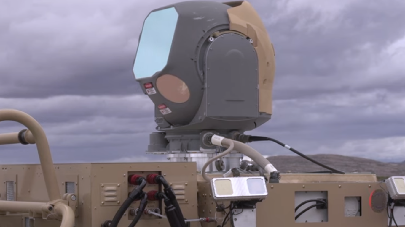 Mounted military laser weapon system with optical sensor turret installed on an armored vehicle under a cloudy sky.