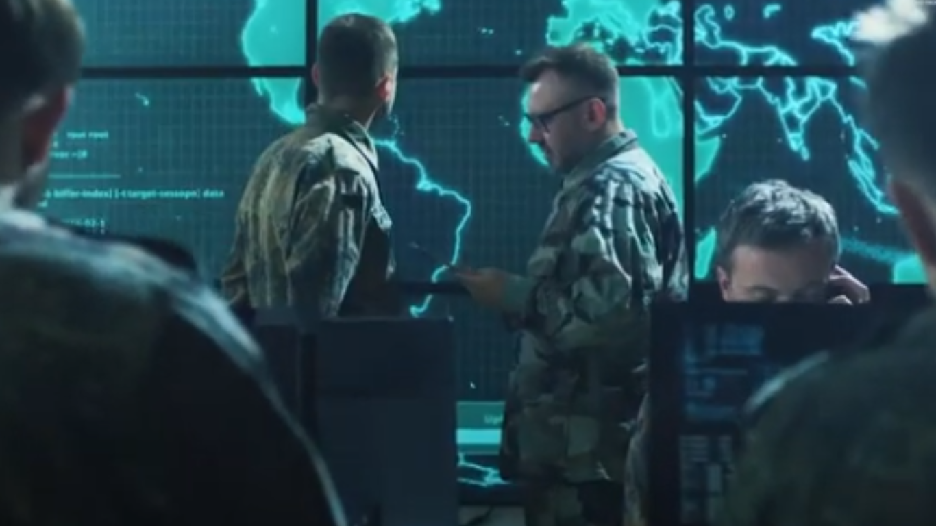 Military analysts in a command center monitoring global map data on large digital screens for geospatial intelligence operations.