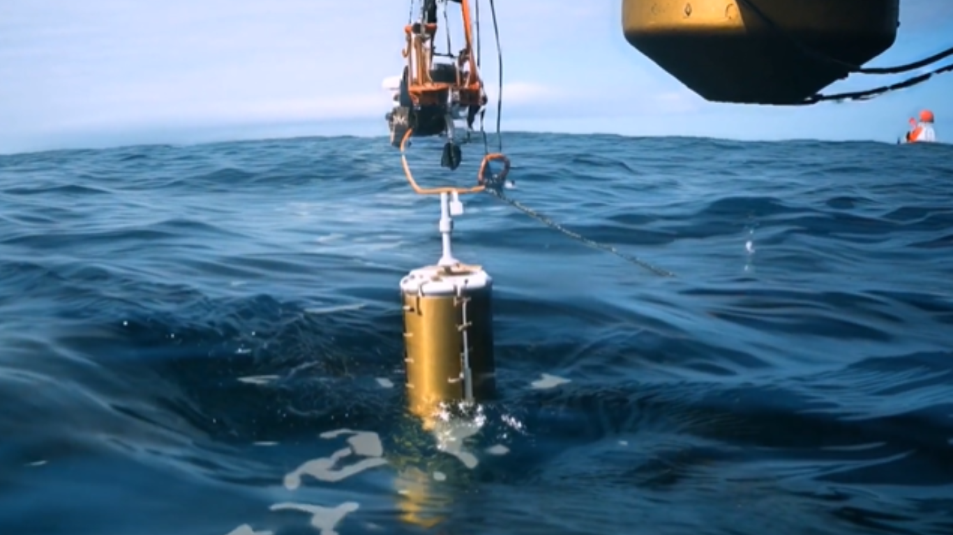 Device being lowered into the ocean from a research vessel, likely an underwater sensor or surveillance instrument collecting marine or environmental data.
