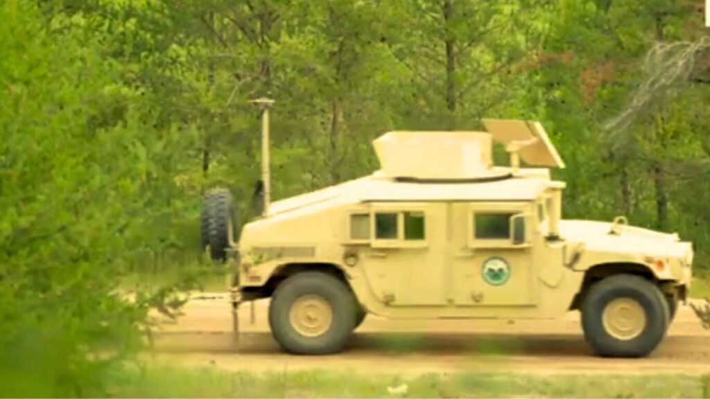 A desert-tan Humvee equipped with roof-mounted satellite hardware driving along a dirt road, illustrating communication support for AI Last Mile Resupply.