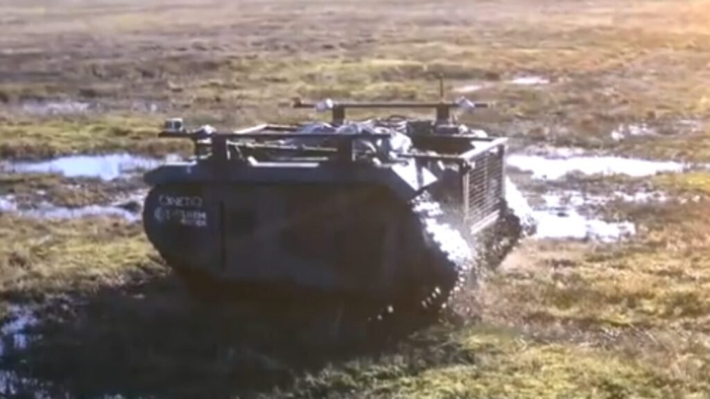 An unmanned tracked vehicle driving through a muddy, marshy field during field testing, highlighting rough-terrain capability for AI Last Mile Resupply.