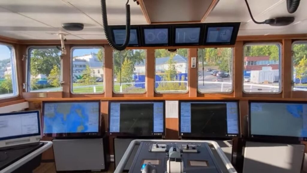 A modern ship bridge with multiple digital navigation screens and windows facing a harbor facility, representing a command hub for AI Powered Unmanned Underwater Vehicles.