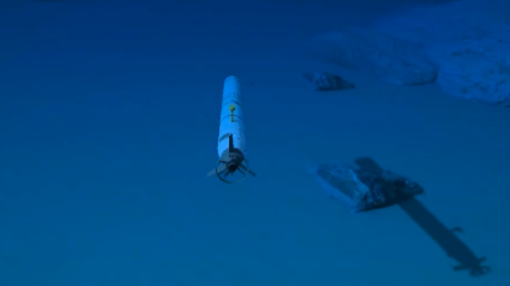 A white torpedo-shaped drone cruising over a sandy seabed, demonstrating the operational path of AI Powered Unmanned Underwater Vehicles.