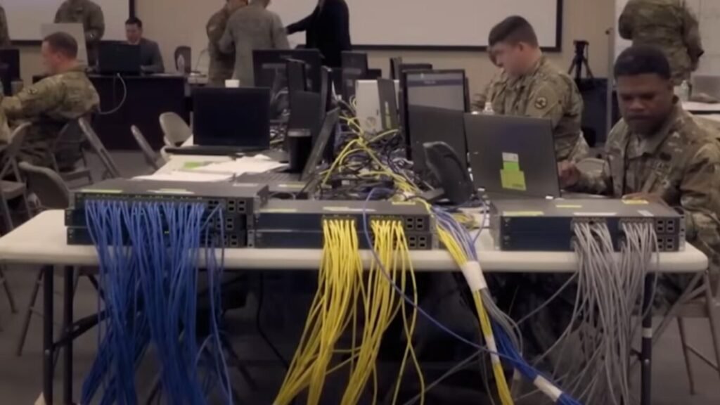 Military personnel setting up networking switches and ethernet cables on a folding table, preparing secure communication infrastructure for the Digital Battlefield.