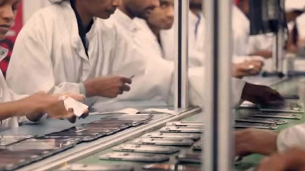 Factory workers in white lab coats assembling smartphones on a production line, highlighting manufacturing supply chains tied to the Digital Battlefield.