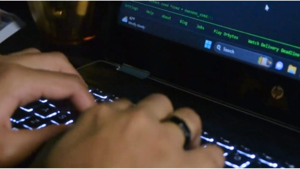 Close-up of hands typing on a backlit laptop keyboard displaying green programming code on the screen, representing Hacktivism 2026.