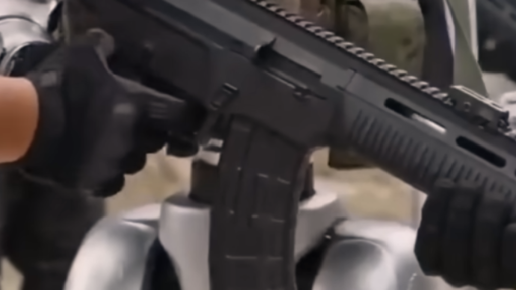 A close-up view of a matte black assault rifle mounted onto a silver mechanical robotic chassis, demonstrating weaponry integration in Military Robotics.