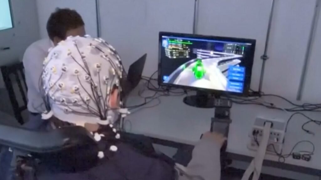 An operator wearing an EEG brain-signal cap controls a digital simulation on a monitor, demonstrating how Neural Link Squad Coordination is changing the way military teams work.