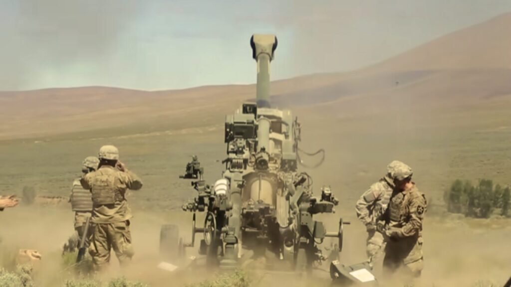 Soldiers firing an artillery piece utilizing a predictive ballistics tracking and targeting system in a desert terrain.