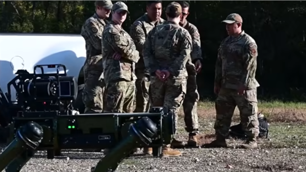 A group of military personnel gathering in a field to discuss a mission beside a robotic quadruped dog, highlighting the use of Q-UGVs in Urban Warfare frameworks.