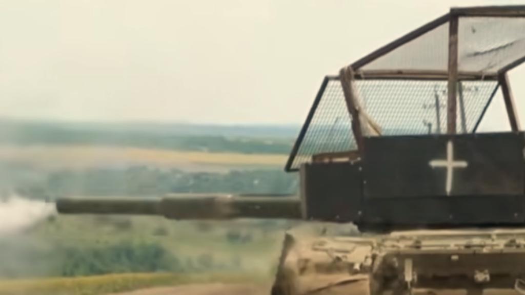 A military tank turret modified with Stealth Ground Drones capabilities, featuring a protective anti-drone mesh cage and a white cross symbol, positioned overlooking an open field.