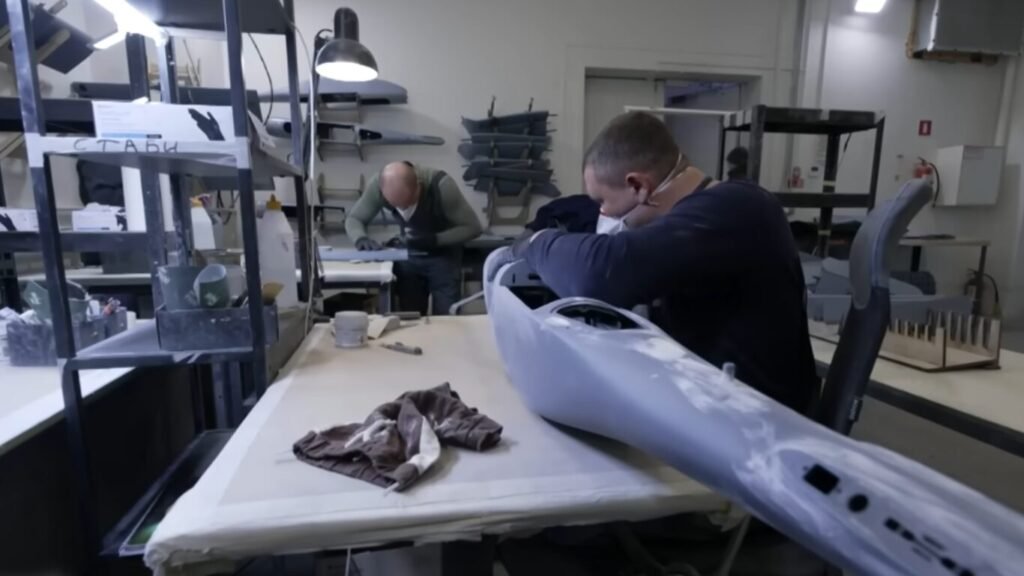 Technicians in a workshop assembly facility working on the fuselage structures of military drones, illustrating the production line behind Swarm Intelligence in Drone Warfare.