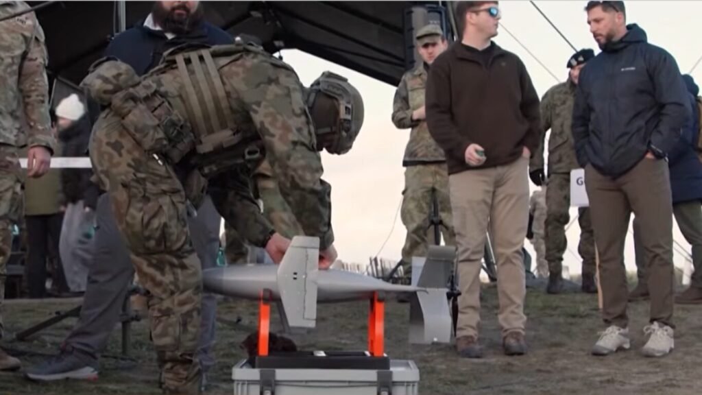 A military operator adjusting a small loitering munition drone on a test stand surrounded by observers, showcasing technology utilized in Swarm Intelligence in Drone Warfare.