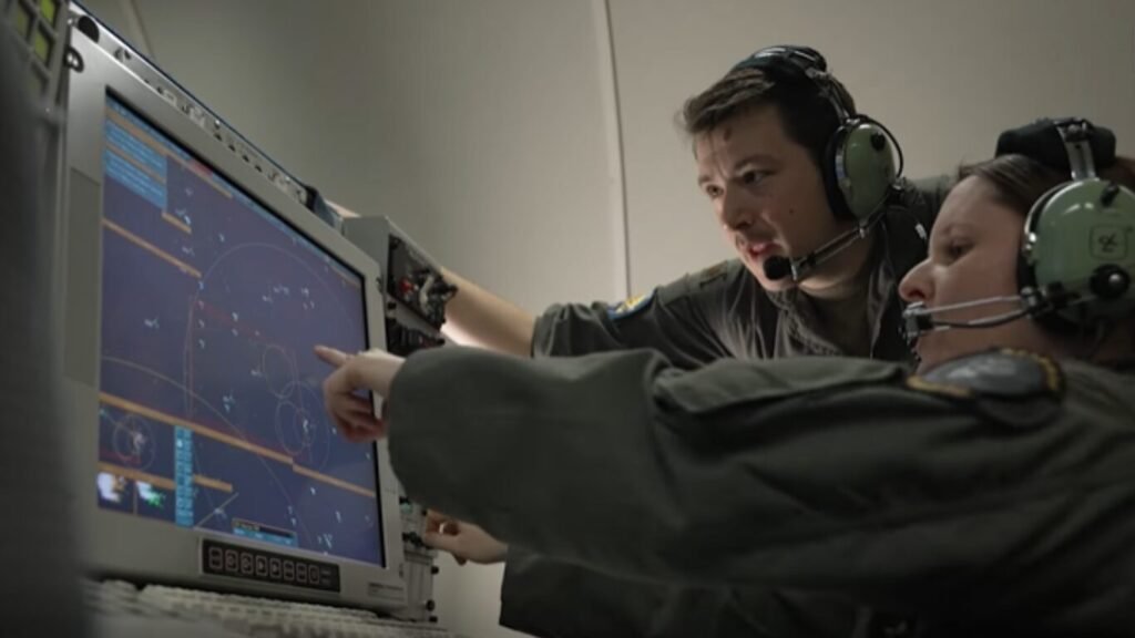 Two military flight operators wearing communication headsets pointing at a radar tracking screen inside an aircraft, demonstrating Tactical AI in Defence Operations.