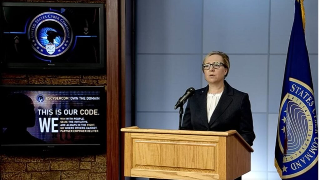 An official podium briefing featuring a spokesperson standing next to the United States Cyber Command seal and a presentation screen displaying the US Cyber Command Strategy 2026.