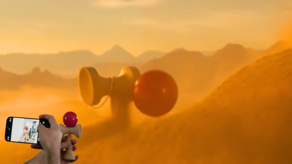 A conceptual visual showing a hand holding a small physical kendama toy while filming it with a smartphone in the lower-left corner, transitioning into a massive, surreal 3D version of the same toy embedded in a dusty desert mountain landscape generated through AI Generative Art.