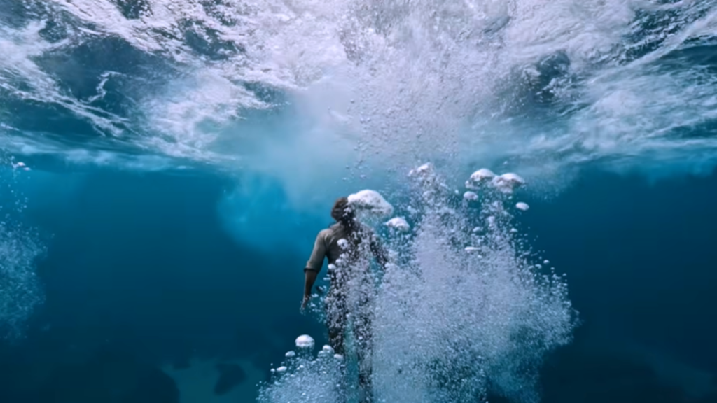 An underwater shot demonstrating an AI Video Transformation, featuring a person swimming downward into deep blue water away from a chaotic trail of white bubbles and a churning ocean surface.