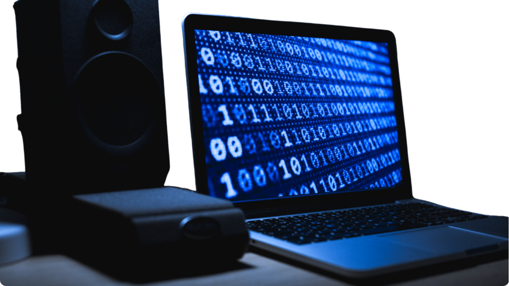 An open laptop displaying glowing blue binary code on its screen next to a dark desktop studio speaker.