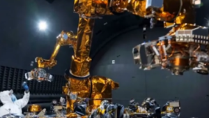 Close-up view of the golden-wrapped dual robotic arms from the Autonomous Satellite Guarding Systems project during testing inside a dark, specialized lab environment with a technician visible on the lower left. U.S. Naval Research Laboratory.