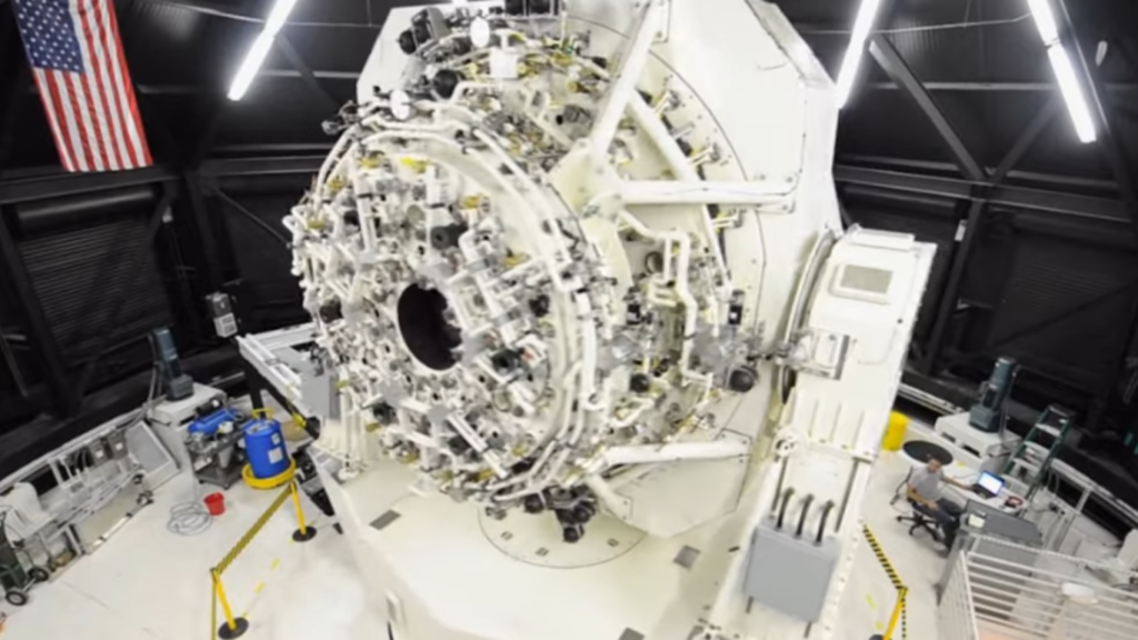 A large, complex white mechanical tracking instrument inside a hangar with an American flag, used to study topics like Space Debris as a Defensive Barrier.